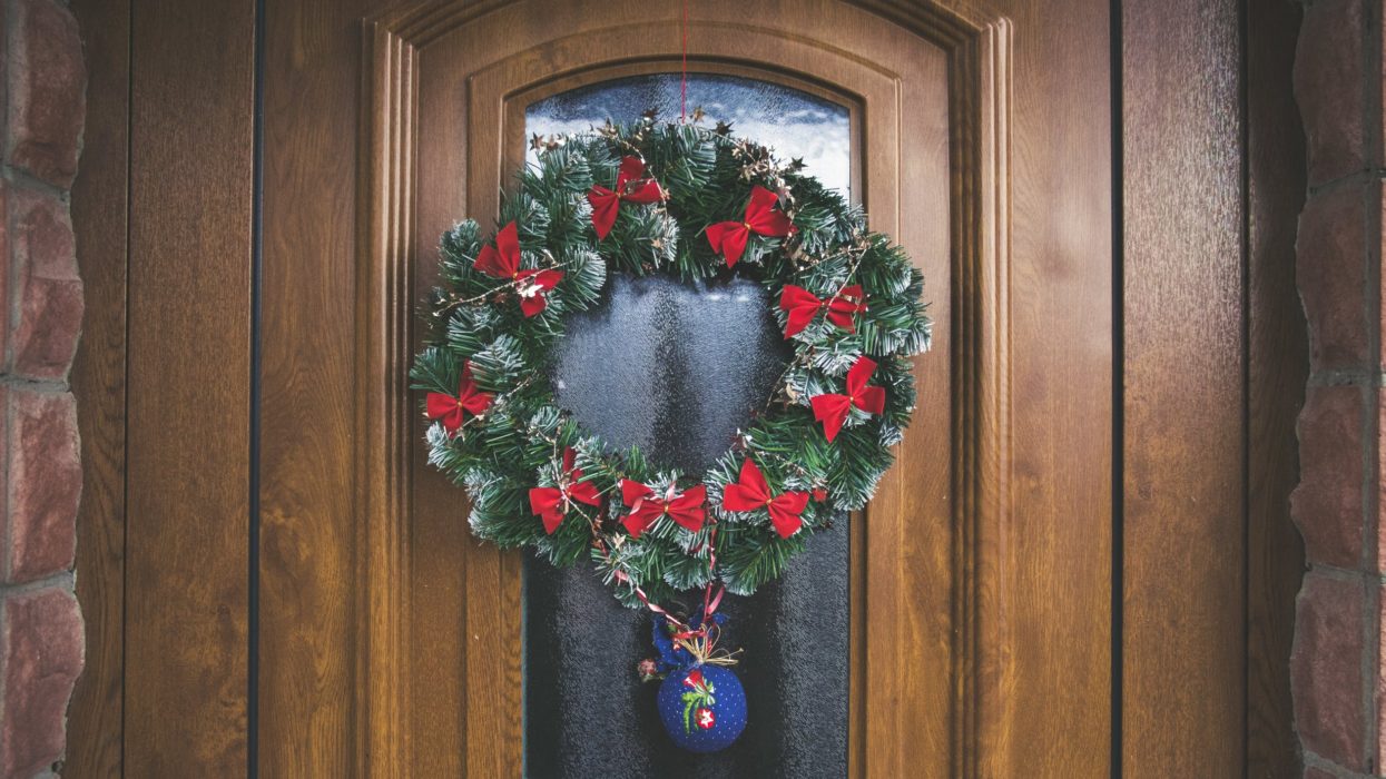 Image of green and red Christmas wreath hanging on a wooden door with frosted glass int he middle of it.